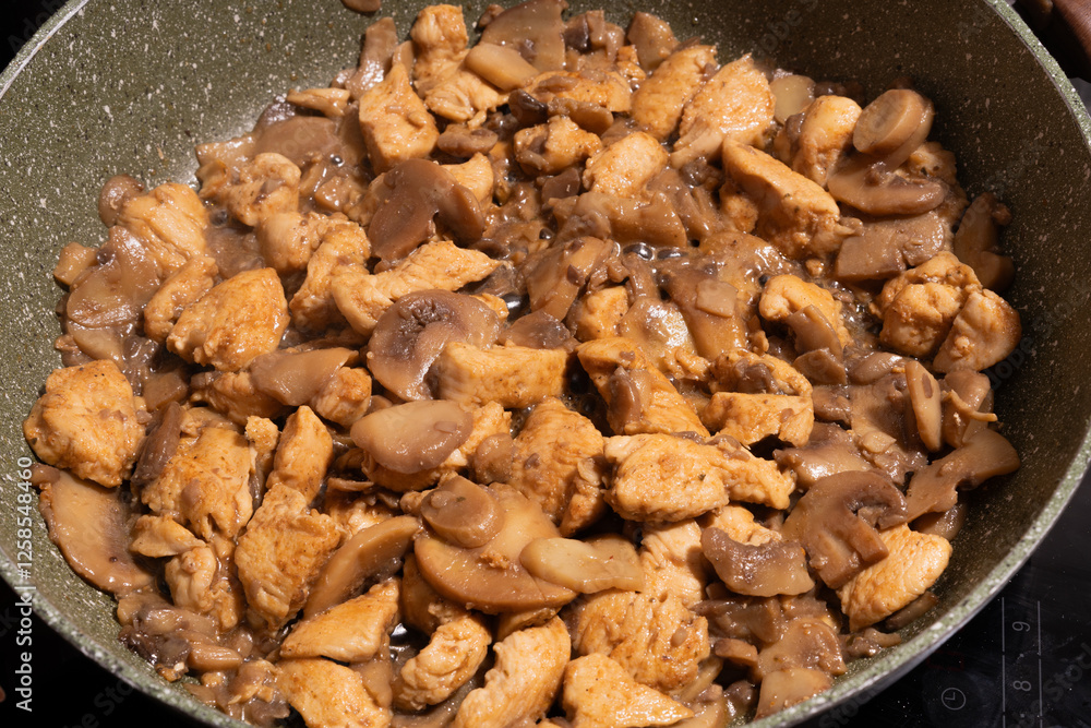A close-up view of a pan filled with cooked chicken pieces and sliced mushrooms.