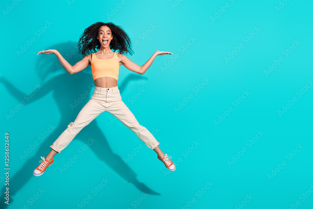 Obraz premium Energetic young woman jumping against a bright teal backdrop, exuding joy and confidence