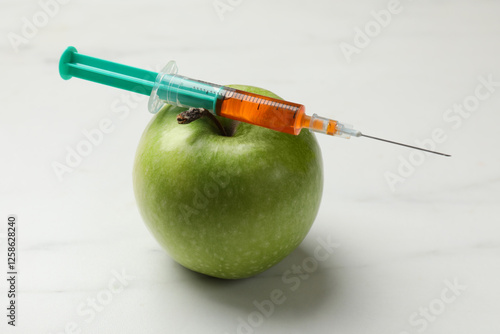 GMO concept. Green apple and syringe on white marble table, closeup
