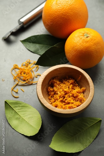 Orange zest, zester tool and fresh fruits on gray textured table, flat lay photo