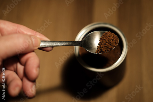 Photos Hand holding teaspoon of instant coffee over container