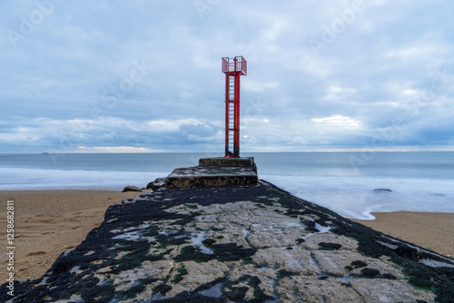 Vue sur la Barre d'Étel avec sa jetée emblématique et sa balise distinctive, sous un ciel dégagé.