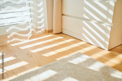 Warm morning sunlight casts striped shadows through sheer curtains onto a natural wooden floor. A soft, cozy rug adds texture and a sense of comfort to the minimalistic interior. The serene and bright photo