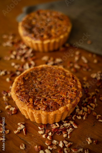 Tartaletas de nuez caramelizada sobre tabla de madera oscura con nueces picadas alrededor