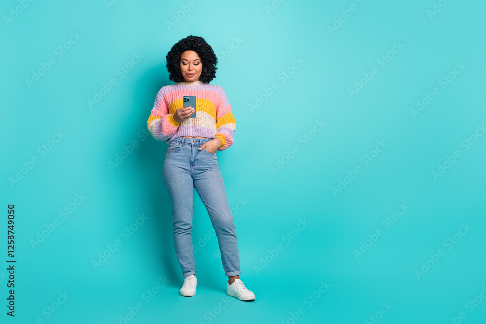 Young stylish woman with curly hair using phone against vibrant turquoise background, wearing a colorful sweater Young stylish woman with curly hair using phone against vibrant turquoise background, wearing a colorful sweater