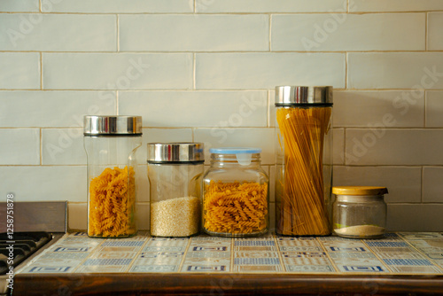 Frascos de almacenamiento de pasta y arroz en cocina rústica con azulejos decorados en blanco y azul, sobre pared blanca