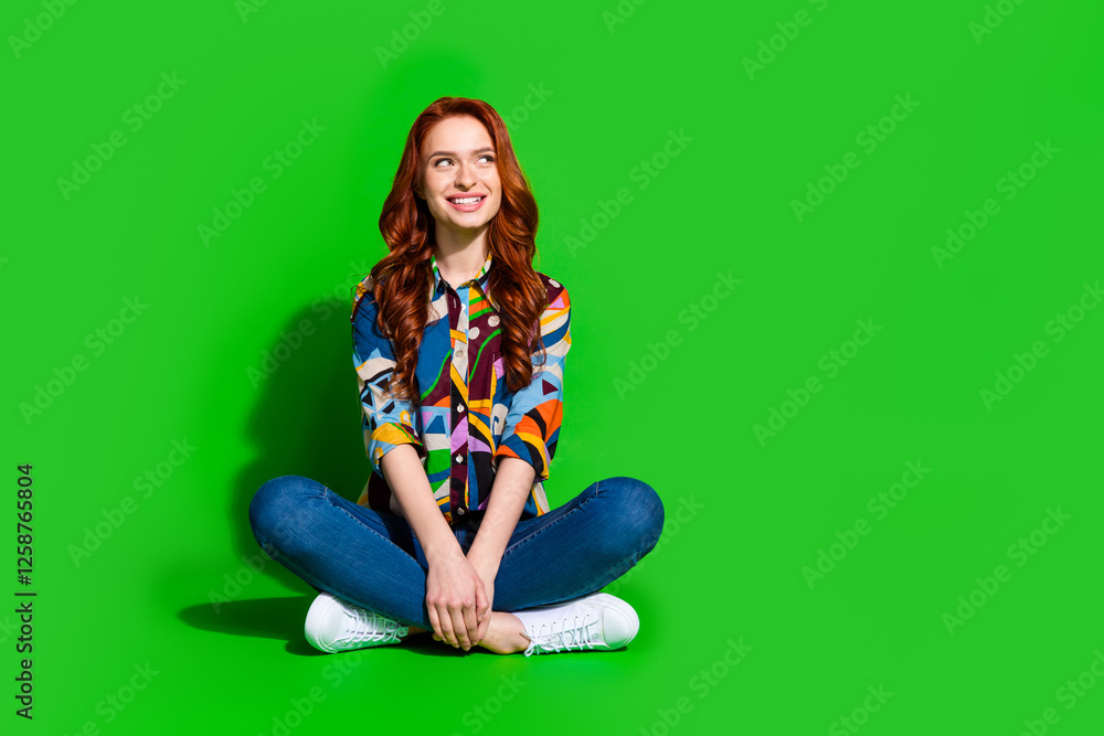 Φωτογραφία Stylish young woman with red hair sitting against a green background, wearing co