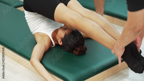 Pilates client practicing leg raises while perform rollover stretch on pilates mat. Woman pose at reverse crunch while trainer helping for strengthen abdominal and improving flexibility. Habituate.