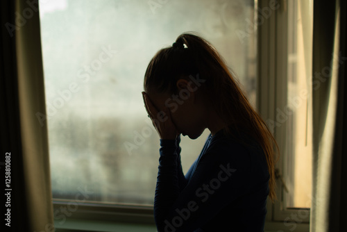 Slika na platnu silhouette of a woman next to apartment window hand over face feeling depressed,