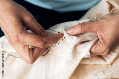Close-up of hands stitching fabric with detailed embroidery, using a needle and thread on white cloth