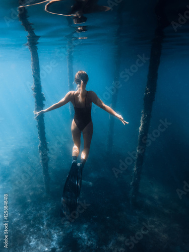 Woman free diver with fins posing under the pier in blue ocean. Female swims under the pier photo