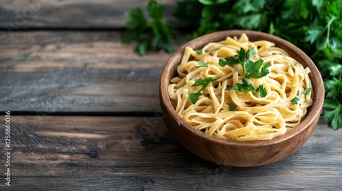 Wooden bowl of fettuccine pasta with parsley on rustic wooden table photo