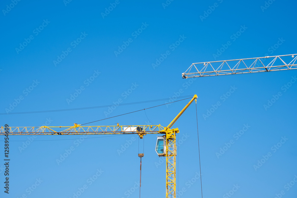 A minimalist shot of two construction cranes set against a vibrant blue sky. The image captures the geometric structure of the cranes, highlighting industrial elements in an urban development setting A minimalist shot of two construction cranes set against a vibrant blue sky. The image captures the geometric structure of the cranes, highlighting industrial elements in an urban development setting