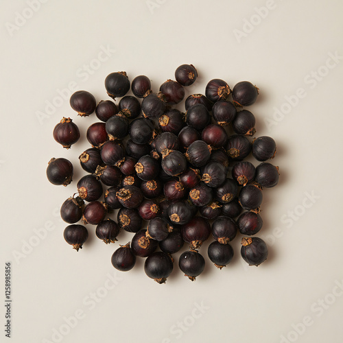 Pile of small, dark purple berries with dried calyxes, scattered on a light beige surface. photo