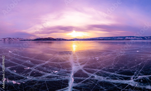 Aerial view on transparent frozen water, violet sunset in background. Beautiful winter landscape with clear blue smooth ice with cracks and mountains. Small Sea, Olkhon, Baikal lake, Siberia, Russia.