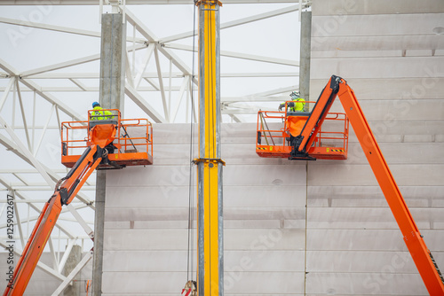 Foto Construction workers working on large scale telescopic boom lift platforms for massive warehouse and factory building
