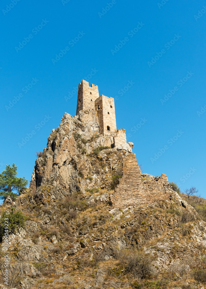 on the tip of a cliff the old stone military tower Vovnushki in Ingushetia, Russia against a blue sky background on the tip of a cliff the old stone military tower Vovnushki in Ingushetia, Russia against a blue sky background