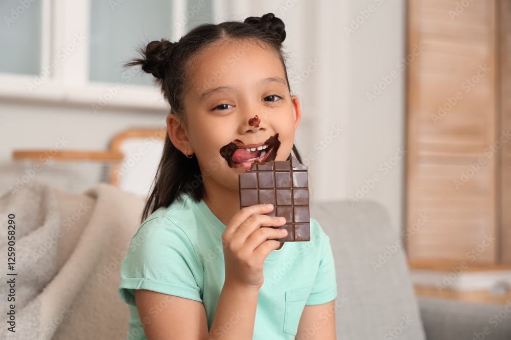 Funny little Asian girl with chocolate bar at home, closeup Funny little Asian girl with chocolate bar at home, closeup