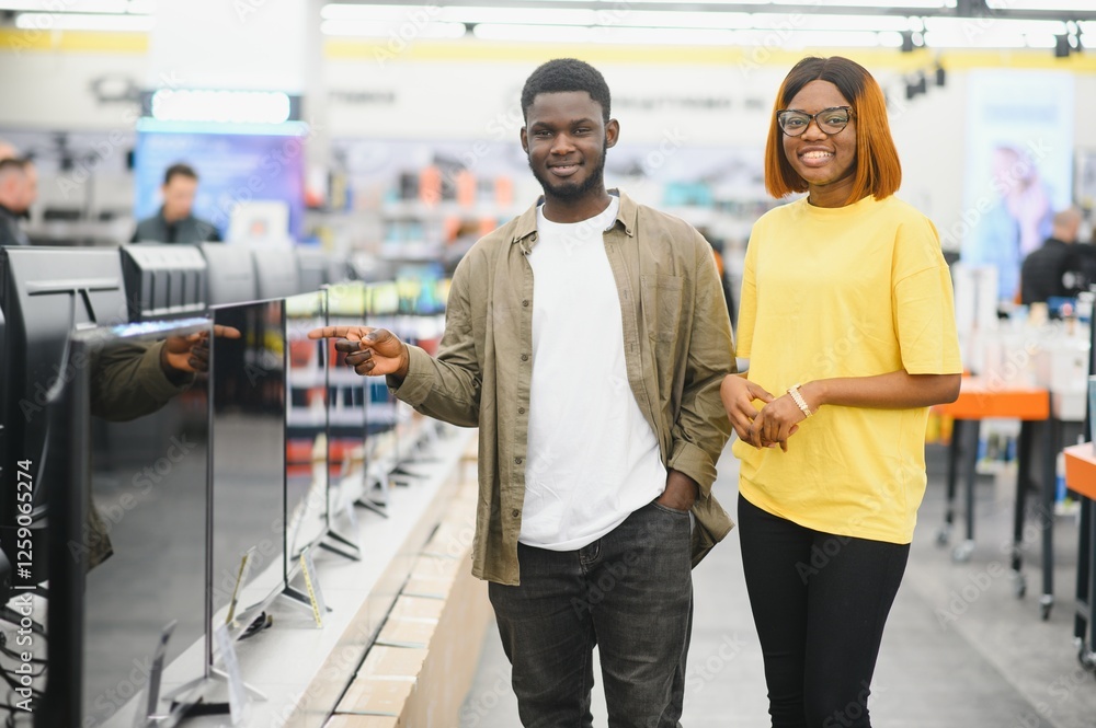 Beautiful couple buying consumer tech products in modern home appliances store. They are choosing home theater and TV devices Beautiful couple buying consumer tech products in modern home appliances store. They are choosing home theater and TV devices