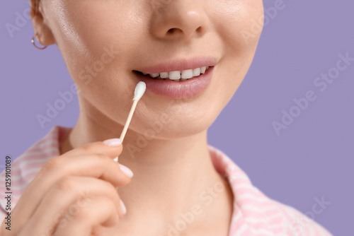 Young woman cleaning lips with cotton bud on lilac background, closeup