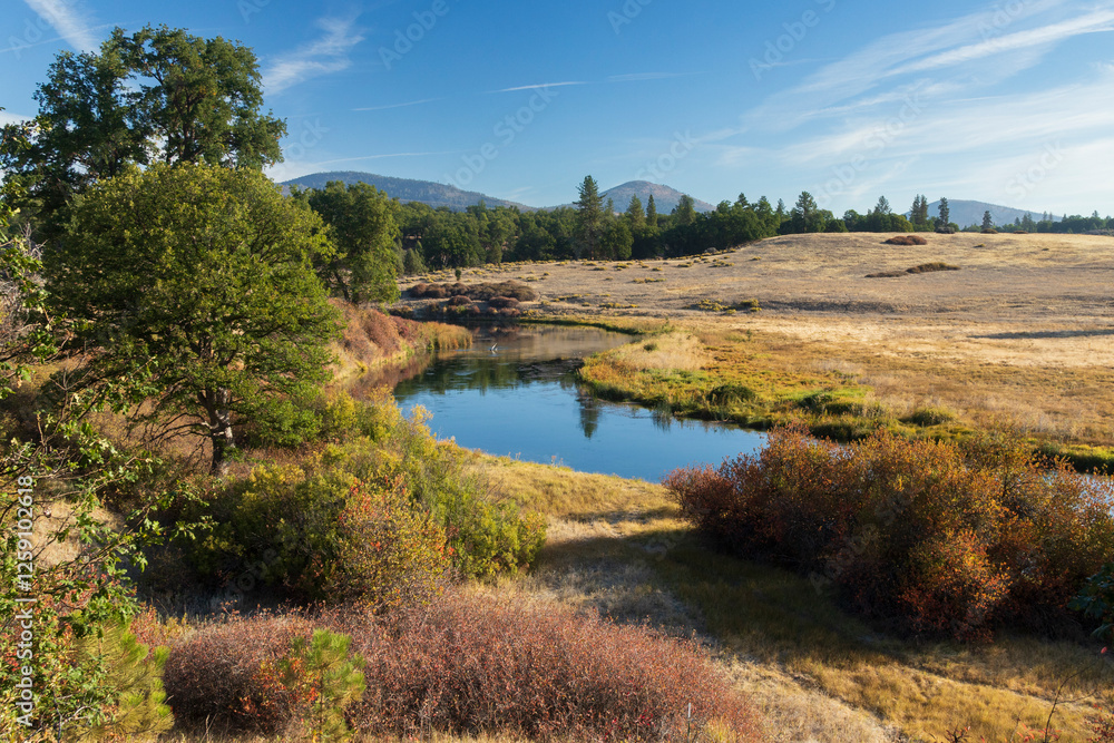 Scenic view of Hat Creek below the Hat 2 powerhouse in Shasta County, California, with calm water, golden grass, and trees on a clear autumn morning. Scenic view of Hat Creek below the Hat 2 powerhouse in Shasta County, California, with calm water, golden grass, and trees on a clear autumn morning.