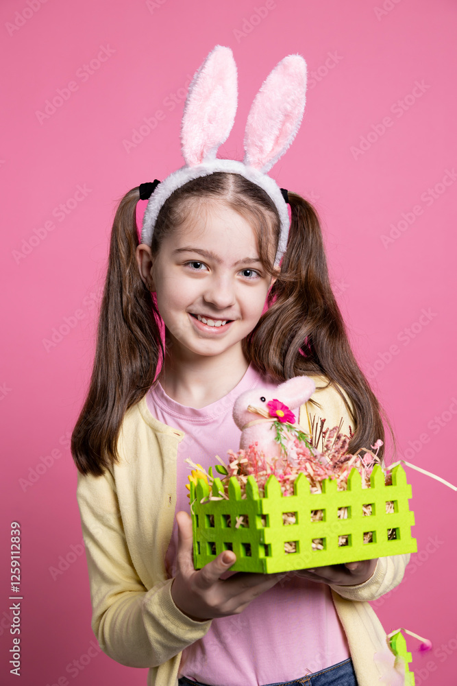 Young smiling kid showing decorated basket with eggs and a rabbit for easter spring celebration event over pink background. Little adorable girl with bunny ears holds colorful decorations. Young smiling kid showing decorated basket with eggs and a rabbit for easter spring celebration event over pink background. Little adorable girl with bunny ears holds colorful decorations.