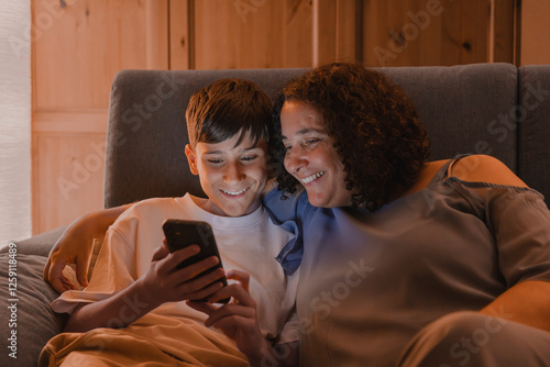 A woman and a boy are sitting on a couch, looking at a cell phone