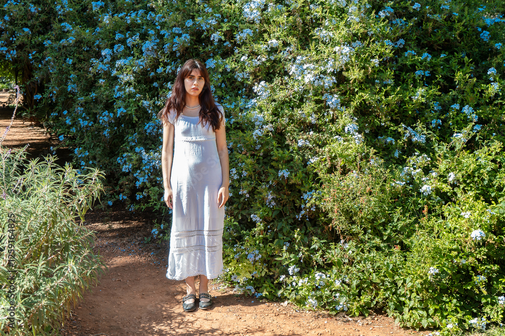 Pregnant woman standing in a blooming garden wearing a white dress Pregnant woman standing in a blooming garden wearing a white dress