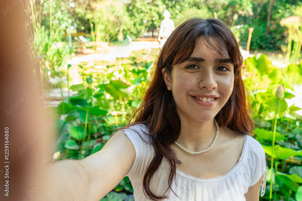 Young woman taking selfie in botanical garden with water lilies Young woman taking selfie in botanical garden with water lilies