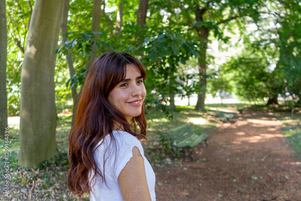 Young woman smiling in green park looking over shoulder Young woman smiling in green park looking over shoulder