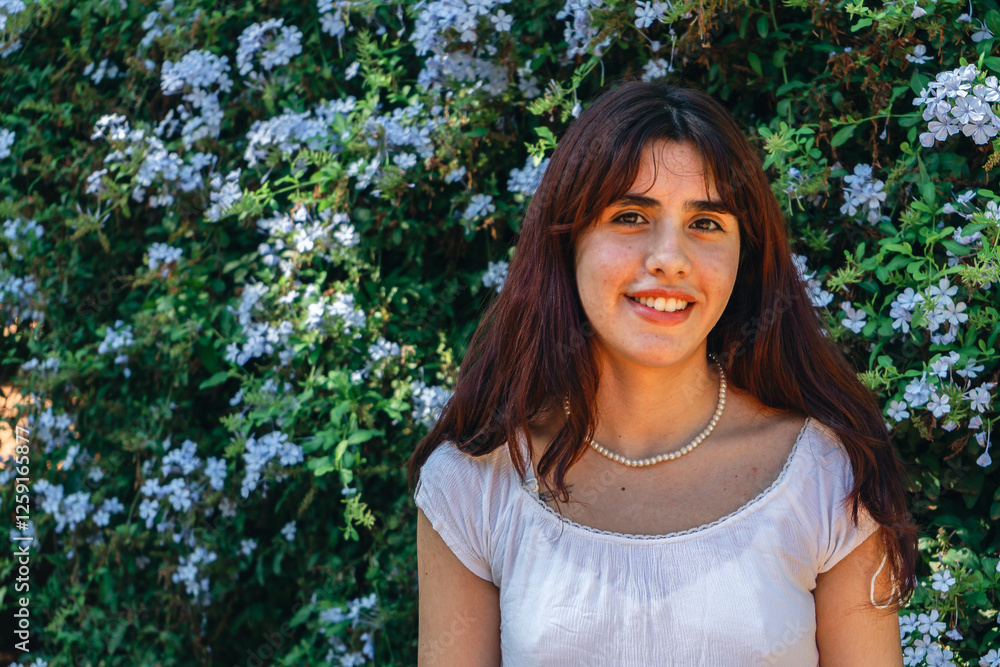 Young woman smiling in front of flowering bush with delicate pearl necklace Young woman smiling in front of flowering bush with delicate pearl necklace