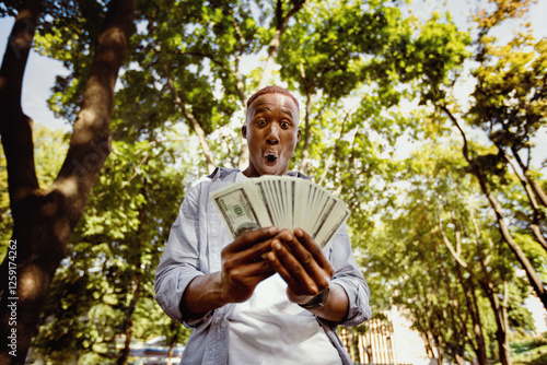 Shocked black guy with huge fan of money at city park photo