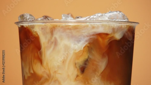 Close-up of iced coffee as creamy milk swirls through the dark liquid.