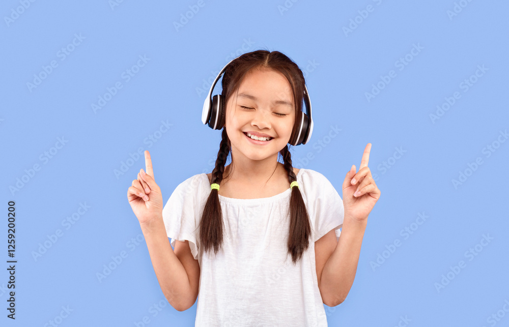 Little Music Lover. Asian Girl In Earphones Enjoying Listening To Song Standing On Purple Studio Background. Little Music Lover. Asian Girl In Earphones Enjoying Listening To Song Standing On Purple Studio Background.