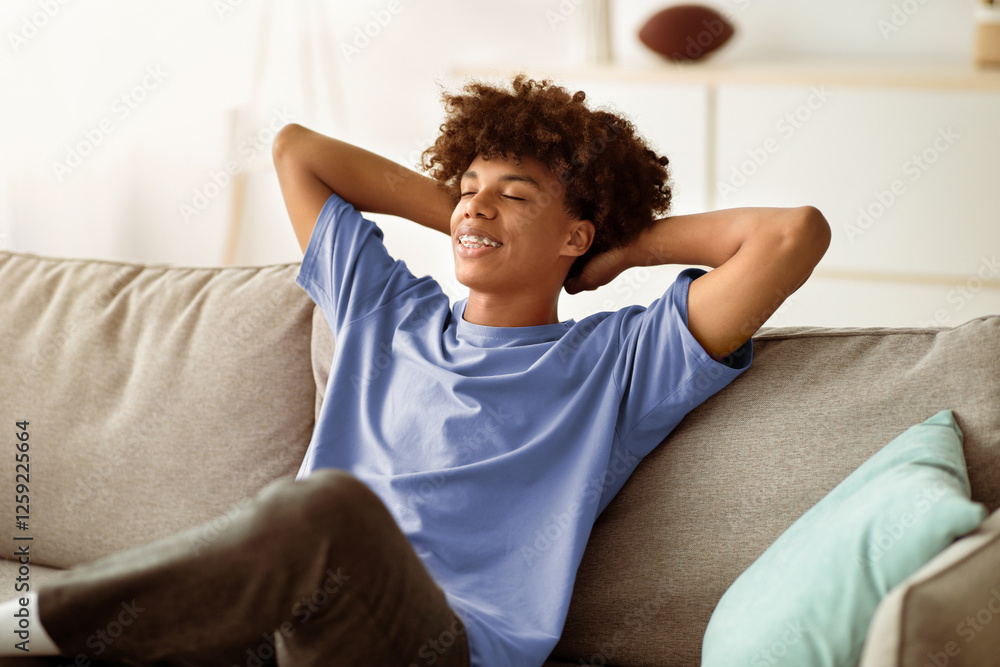 Cheerful black teenager relaxing on comfy couch at home during covid quarantine. Peaceful African American adolescent resting on sofa, spending lazy time on weekend morning Cheerful black teenager relaxing on comfy couch at home during covid quarantine. Peaceful African American adolescent resting on sofa, spending lazy time on weekend morning
