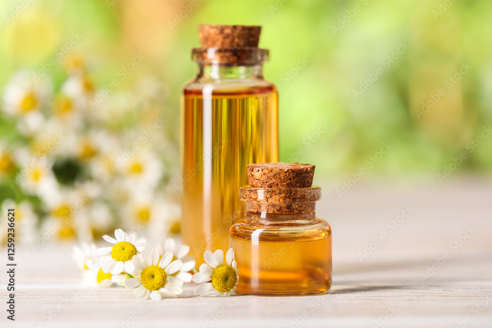 Bottles of essential oil and chamomile flowers on white wooden table against blurred background, closeup Bottles of essential oil and chamomile flowers on white wooden table against blurred background, closeup