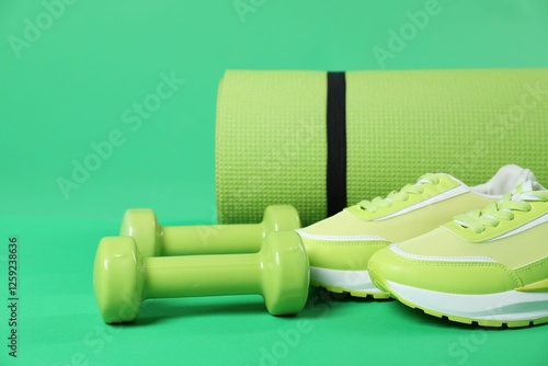 Fitness mat, sneakers and dumbbells on green background, closeup. Sports equipment photo