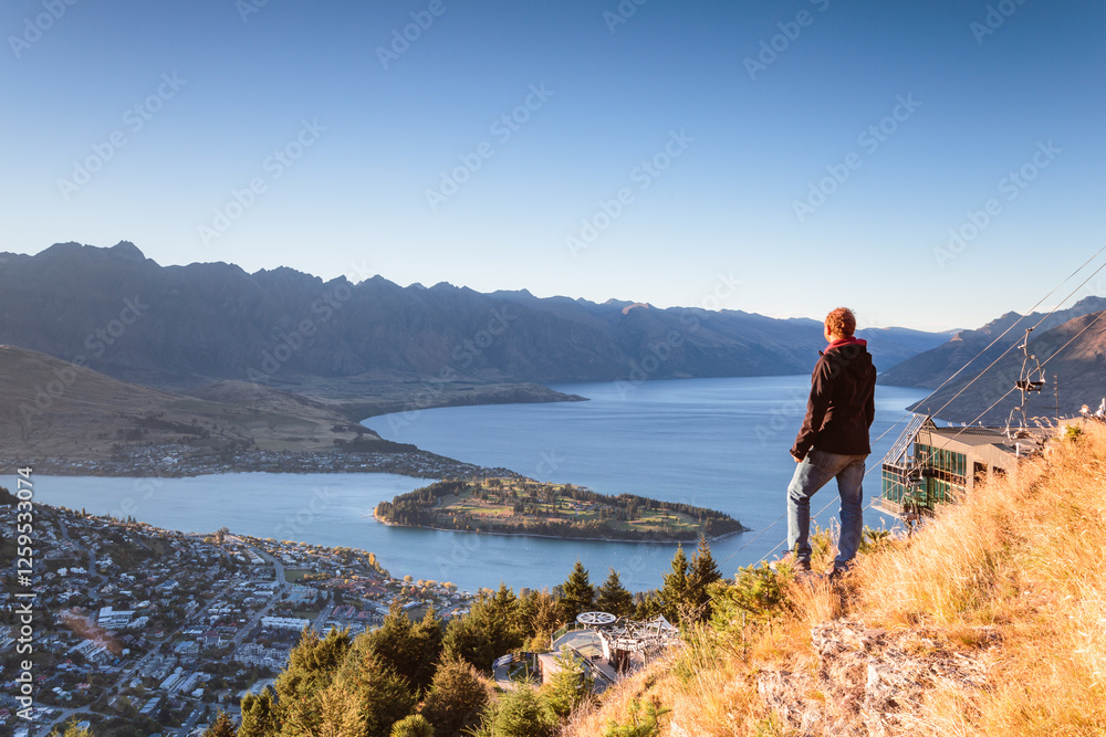 Adult man looking at Queenstown from lookout at sunrise, New Zealand Adult man looking at Queenstown from lookout at sunrise, New Zealand