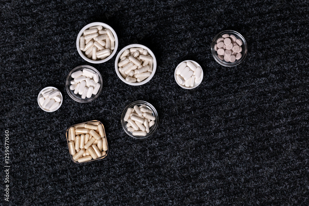Dietary supplements, many vitamins and minerals in small plates and jars on black background from above. Big amount of white colored pills and nutritional supplements, top view. Healthy lifestyle Dietary supplements, many vitamins and minerals in small plates and jars on black background from above. Big amount of white colored pills and nutritional supplements, top view. Healthy lifestyle