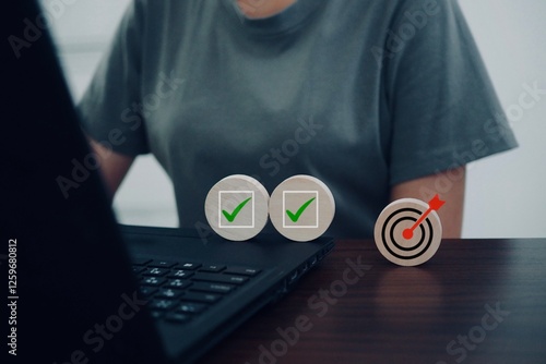 A woman is using a computer, and a round wooden stick with a checkmark and a target is placed on the table.