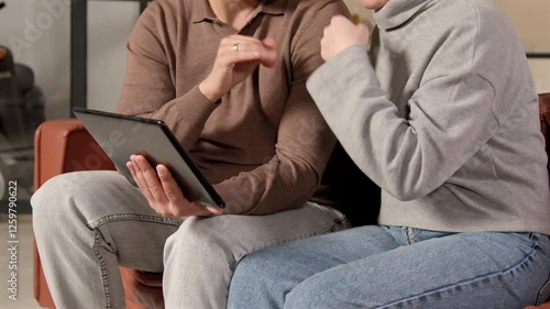 Wallpaper Mural Close-up of mature couple with hearing loss sitting on sofa, networking , browsing and discussing social media content online with sign language using digital tablet indoors. Torontodigital.ca