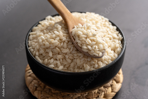 Macro photography of white short grain rice in wooden spoon on dark background. Short white rice in wooden spoon. Closeup photo of rice. 