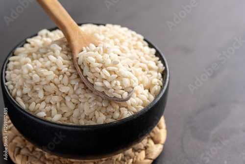 Macro photography of white short grain rice in wooden spoon on dark background. Short white rice in wooden spoon. Closeup photo of rice. 