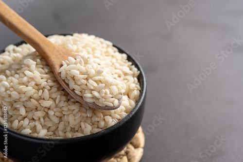 Macro photography of white short grain rice in wooden spoon on dark background. Short white rice in wooden spoon. Closeup photo of rice. 