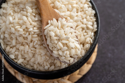 Macro photography of white short grain rice in wooden spoon on dark background. Short white rice in wooden spoon. Closeup photo of rice. 