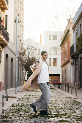 Young stylish woman with a reusable coffee cup dancing and having fun on the street