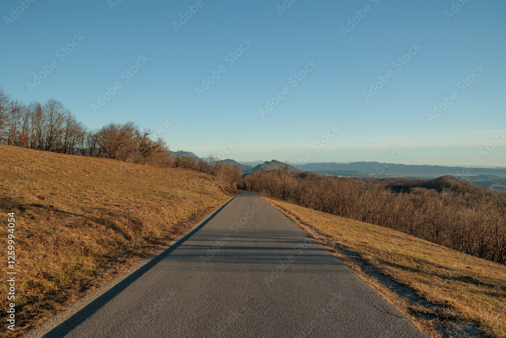 panoramica su di un ambiente naturale collinare in Slovenia, in cima ad una collina, visto da lungo una strada alta, asfaltata, in discesa, in inverno, con cielo sereno
