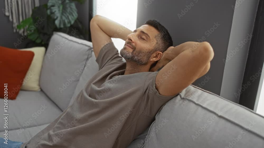 Young man relaxing on couch at home with hands behind head in a cozy living room featuring neutral colors and modern decor embodying a serene indoor atmosphere Young man relaxing on couch at home with hands behind head in a cozy living room featuring neutral colors and modern decor embodying a serene indoor atmosphere