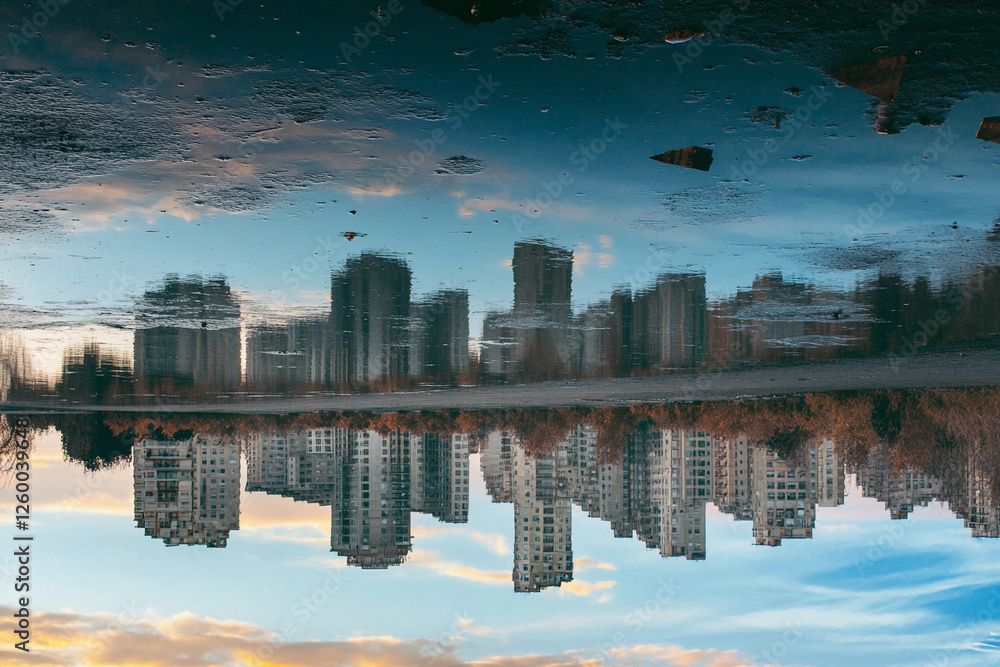 Fototapeta premium City skyline reflects in calm lake surrounded by trees during sunset with vibrant clouds and soft glow