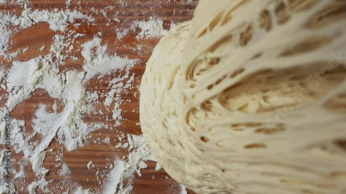 A highly detailed close-up of fermented dough being lifted, revealing an intricate network of air pockets and gluten strands. The dough is elastic and porous, with a well-developed structure